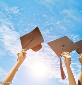 Four hands holding graduation hats on background of blue sky.